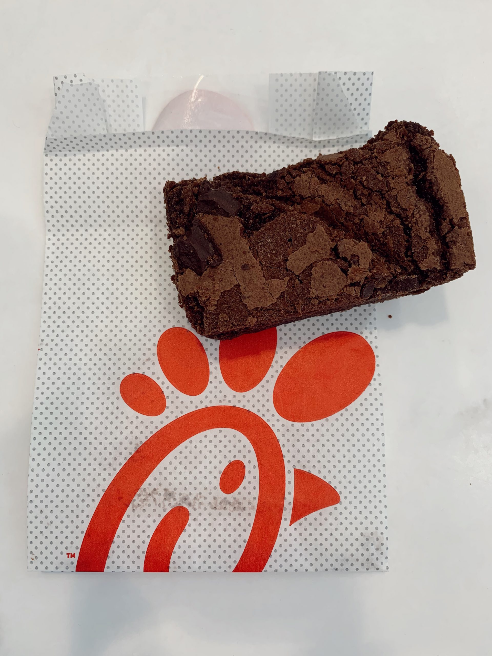 A fresh-baked, fudgy, chocolate brownie sits on top a Chick-fil-A treat bag with the red logo.